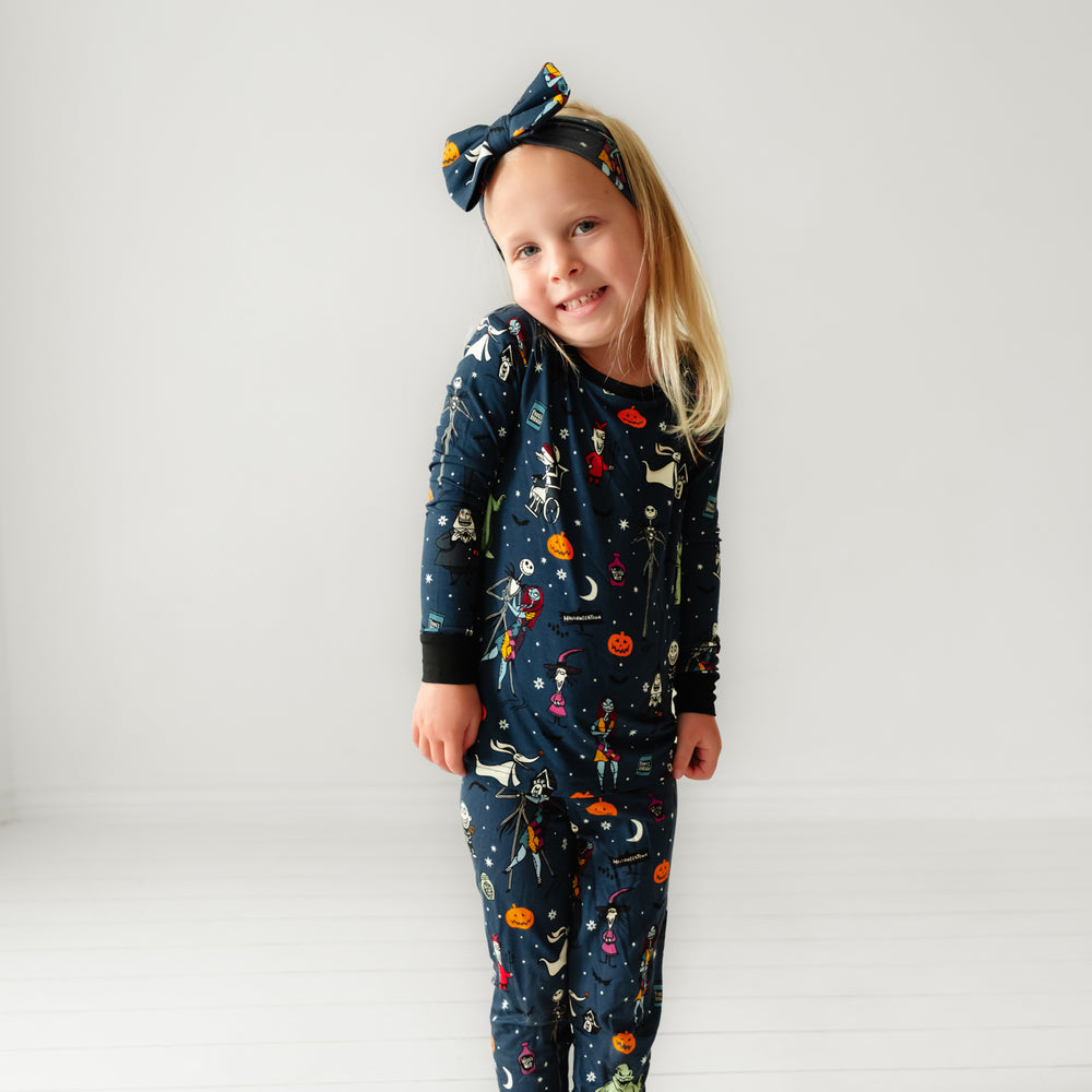 Click to see full screen - Child wearing a Jack Skellington and Friends printed two-piece pajama set and matching luxe bow headband
