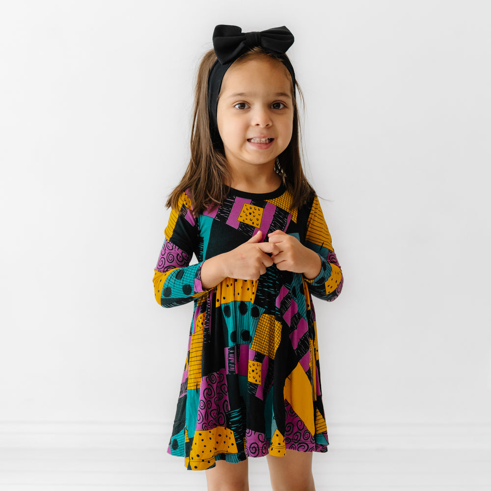 Child wearing a Sally's Patchwork twirl dress with bodysuit and coordinating black luxe bow headband