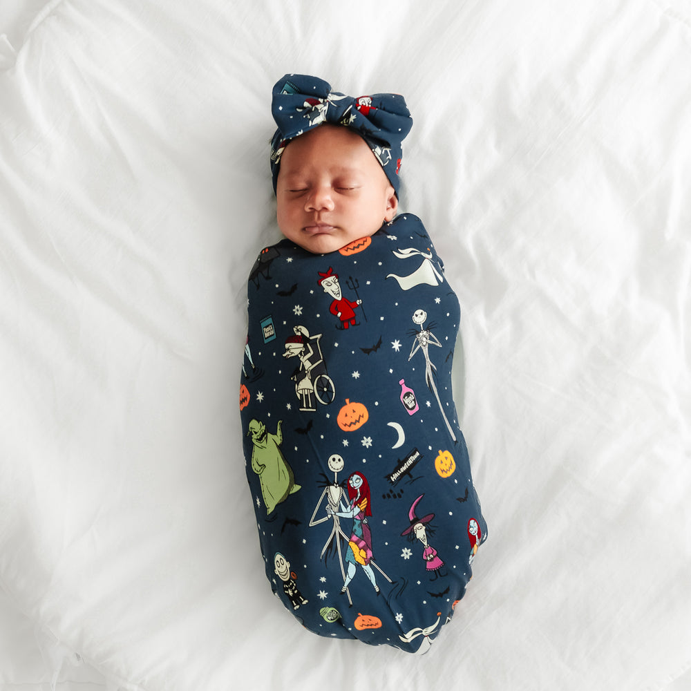 Alternate image of a child laying on a blanket in a Jack Skellington and Friends printed swaddle and luxe bow headband set