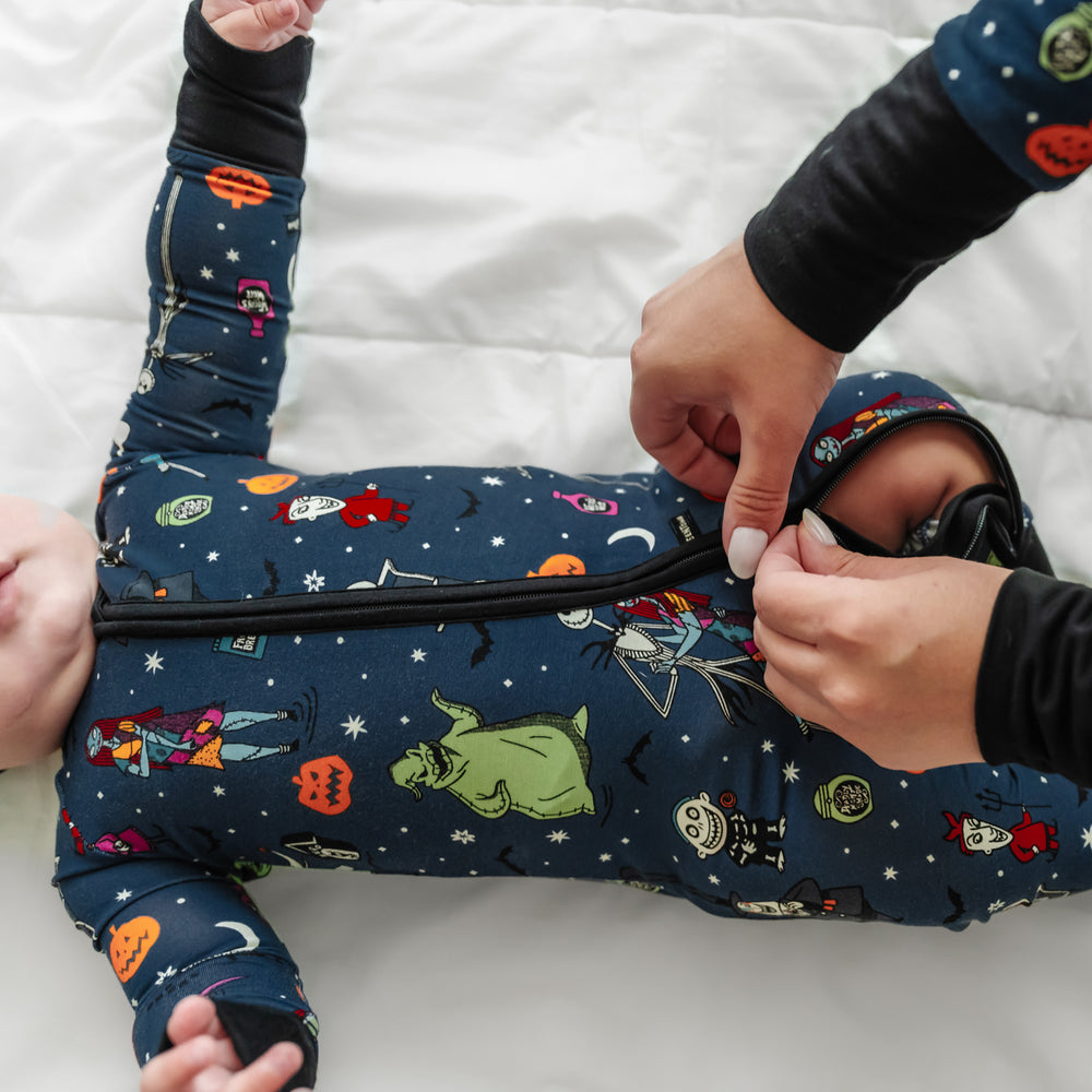Click to see full screen - Close up image of a child laying on a bed wearing a Jack Skellington and Friends printed zippy with a parent zipping it closed