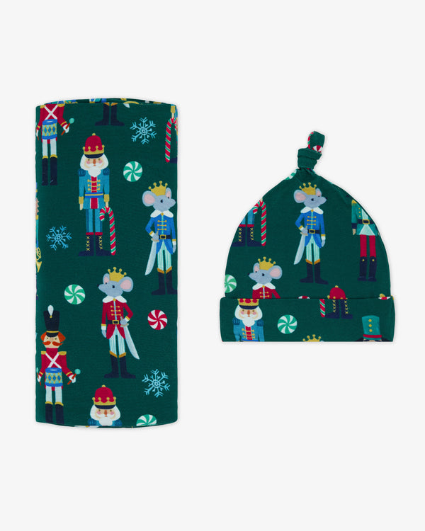 Flat lay of baby wearing the Nutcracker March Swaddle & Hat Set