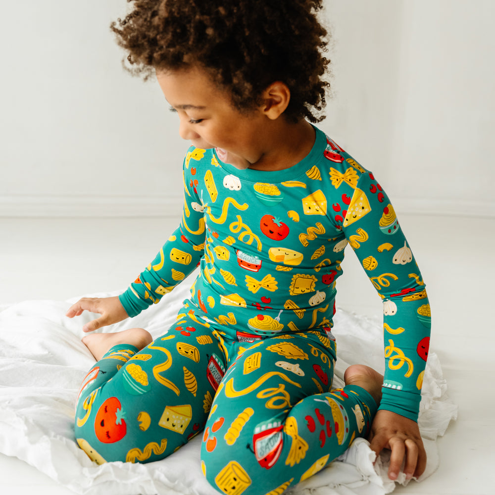 Click to see full screen - Child kneeling on a blanket laughing wearing a Pasta Party two-piece pajama set