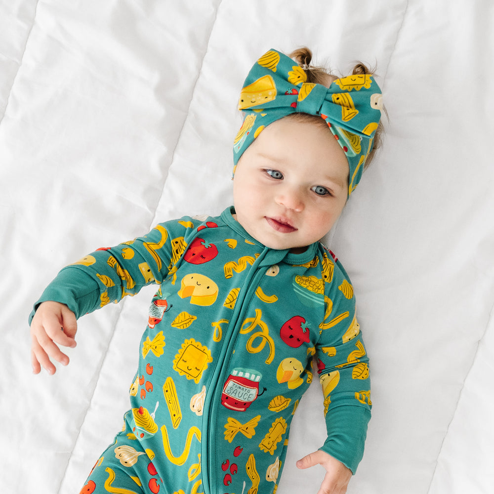 Click to see full screen - Child laying on a blanket wearing a Pasta Party luxe bow headband and matching pajamas
