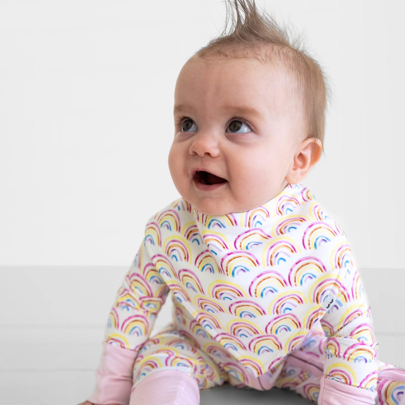 Close up of a child wearing a Pastel Rainbows baby bandana bib over matching bamboo pajamas