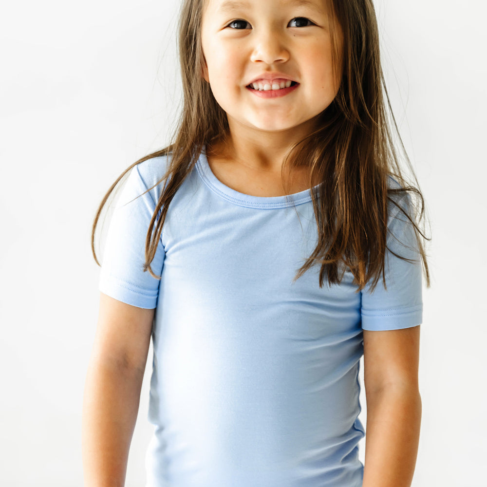 Close up image of a child posing wearing a Periwinkle Blue two piece short sleeve and shorts pajama set focusing on the short sleeve pajama top