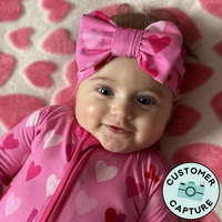 Customer Capture image of a child wearing a pink xoxo luxe bow headband and matching zippy