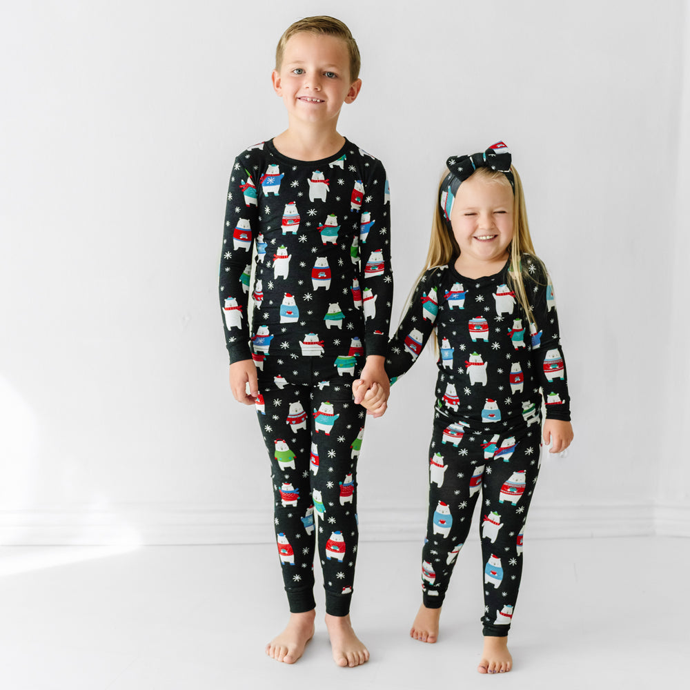 Click to see full screen - Two siblings wearing matching Polar Bear Pals two piece pajama sets. One child pairs her pjs with a matching luxe bow headband 