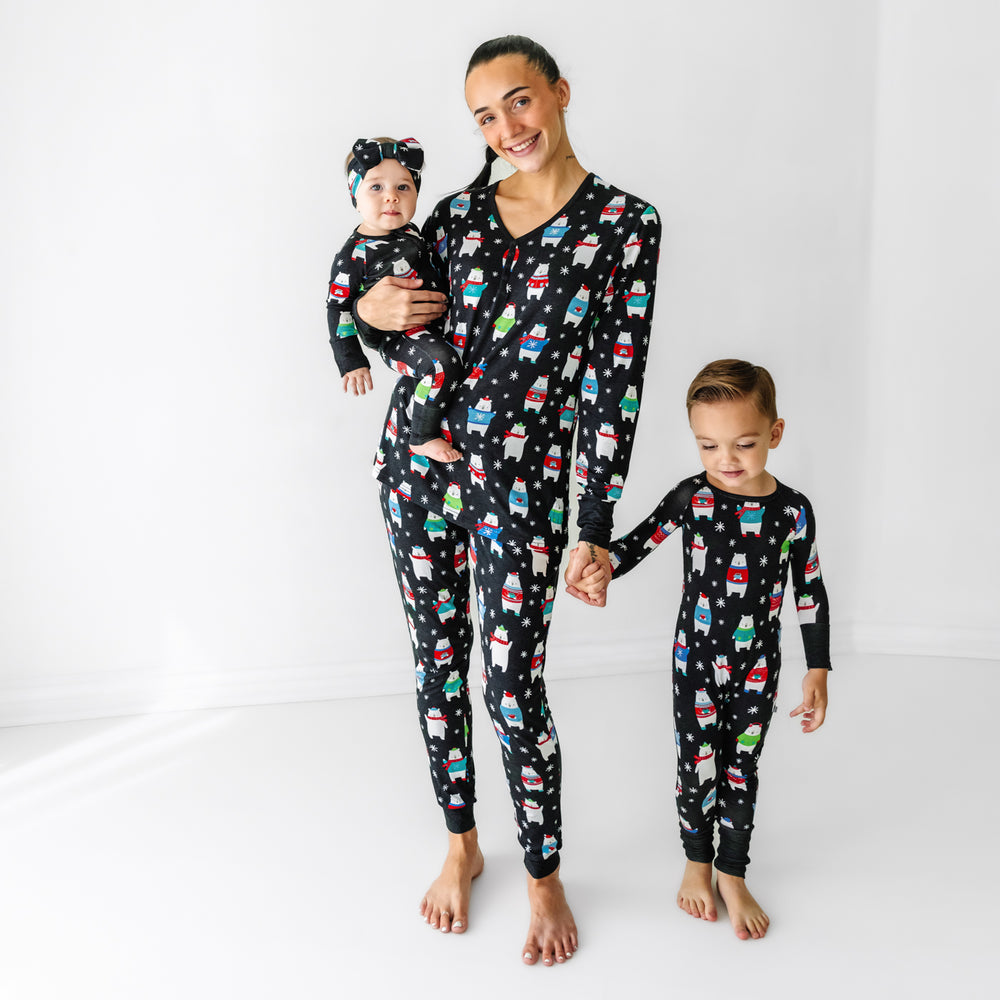 Mother and her two children posing wearing matching Polar Bear Pals pajamas. Mom is wearing Polar Bear Pals women's pajama top paired with matching women's pajama pants. Her children are wearing Polar Bear Pals printed pajamas in two piece pajama set and zippy styles paired with a matching luxe bow headband.