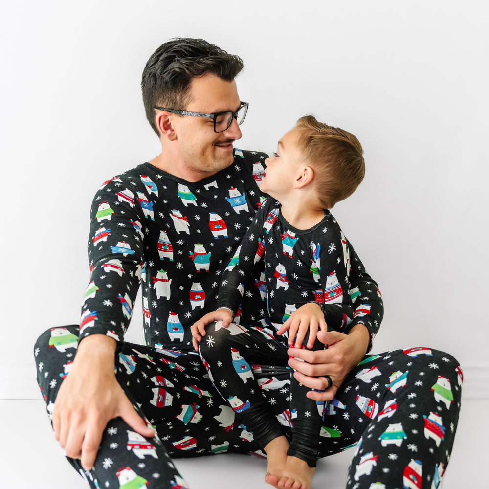 Father and son cuddling wearing matching Polar Bear Pals pajamas. Dad is wearing Polar Bear Pals men's pajama top paired with matching men's pajama pants. Child is wearing Polar Bear Pals two piece pajama set