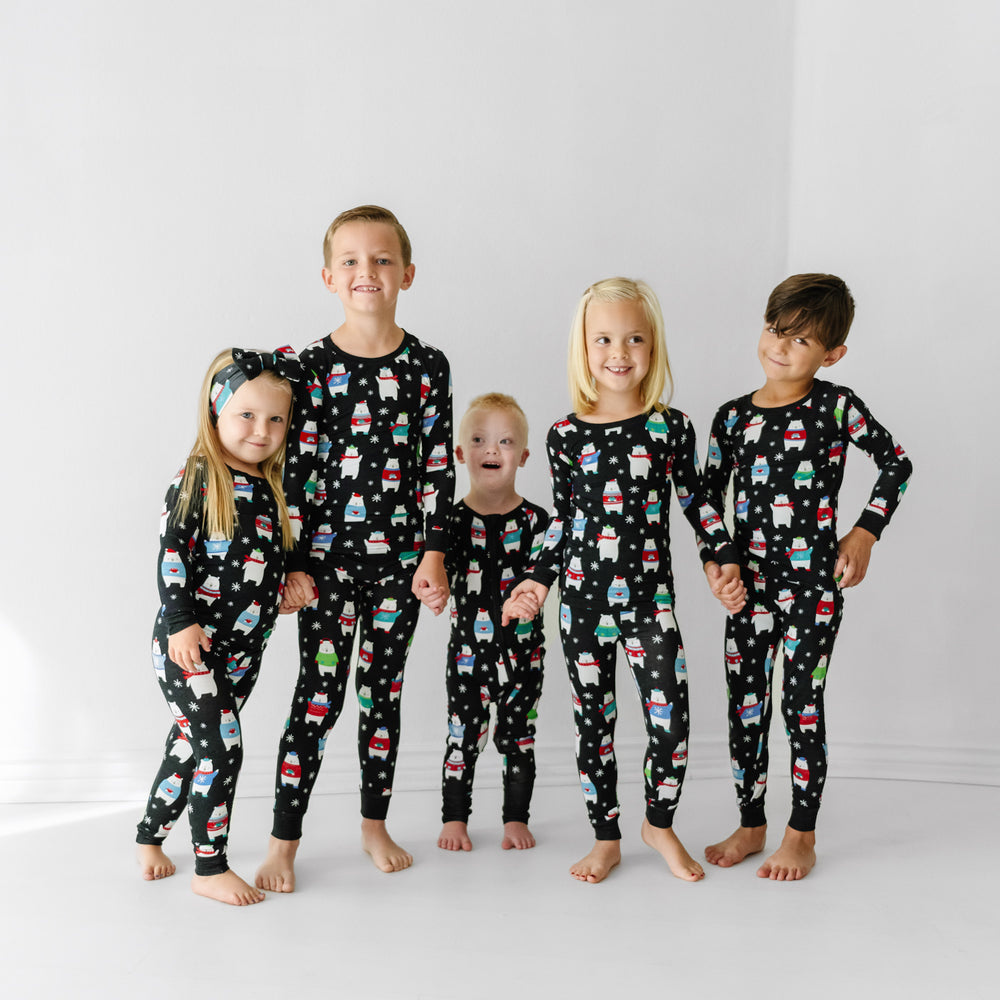 Click to see full screen - Five children holding hands together wearing matching Polar Bear Pals pajamas in zippy and two piece styles paired with a luxe bow headband