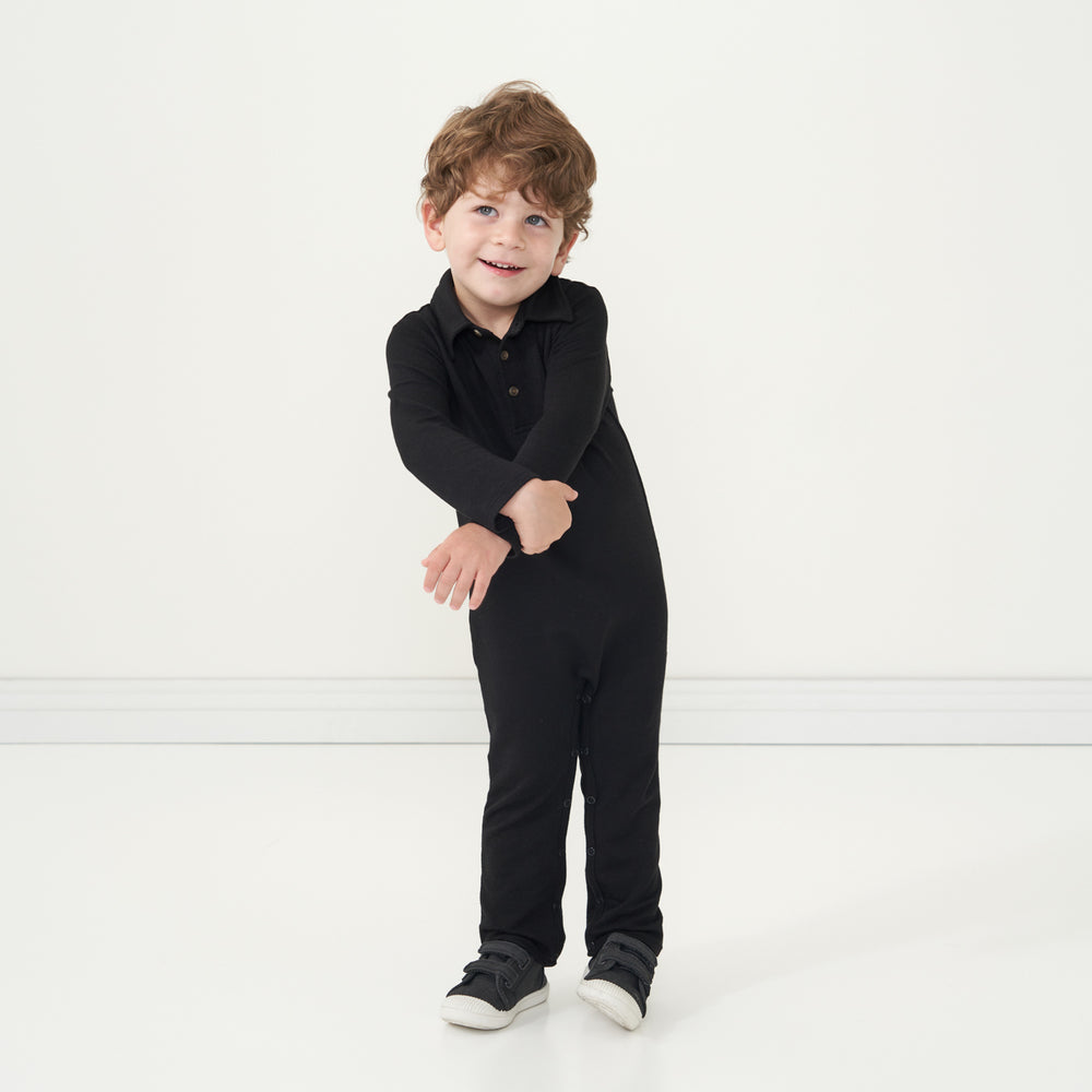 Child holding their arm wearing a Black polo romper