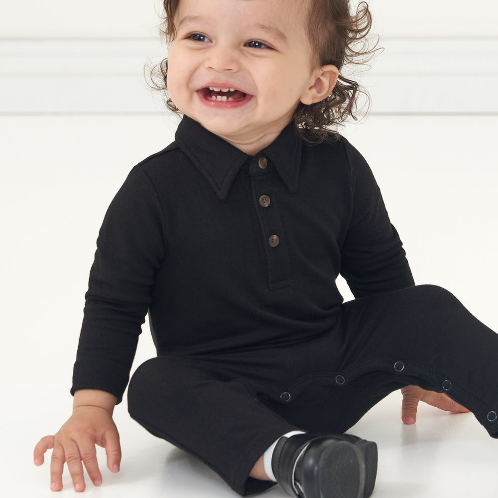 Child sitting on the ground wearing a Black polo romper