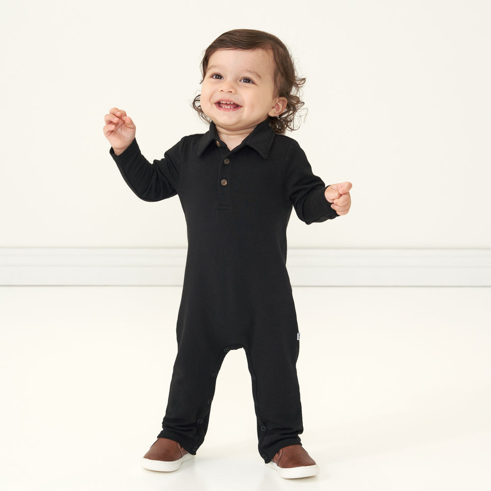 Child wearing a Black polo romper and laughing