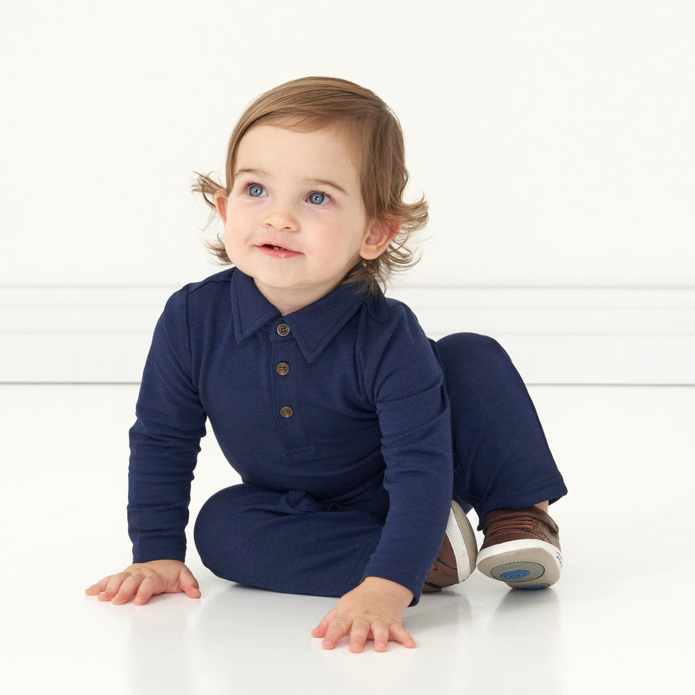 Child sitting on the ground wearing a Classic Navy polo romper