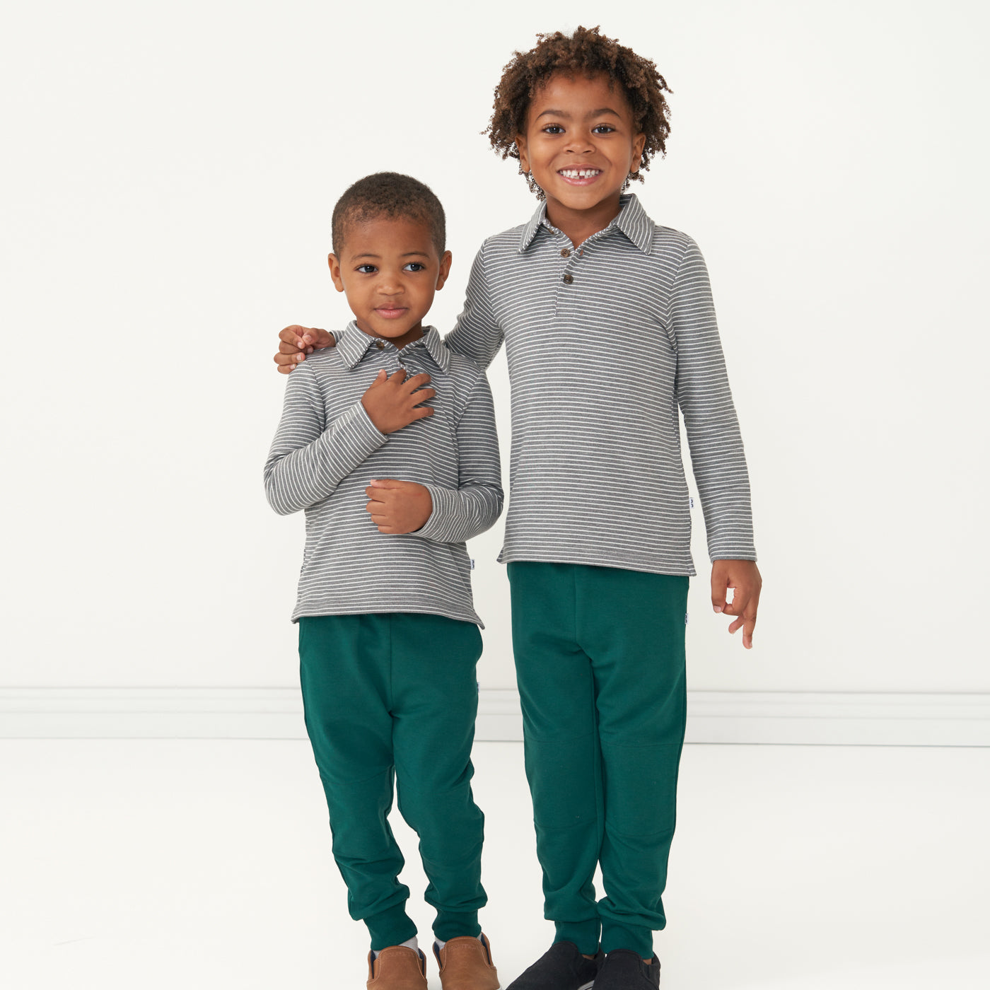 Two children matching wearing Heather Charcoal stripes polo shirts paired with Emerald joggers