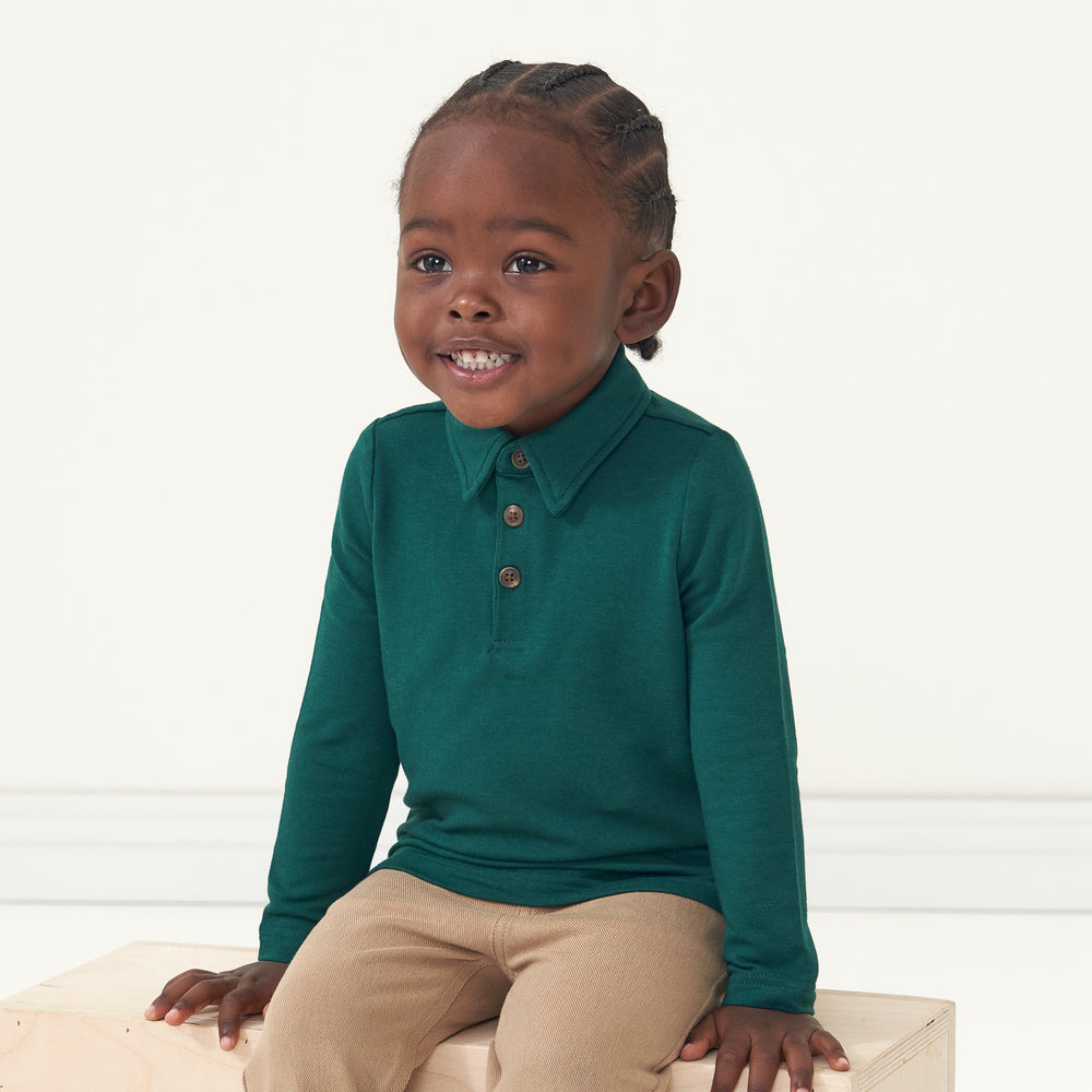 Child sitting wearing an Emerald polo shirt