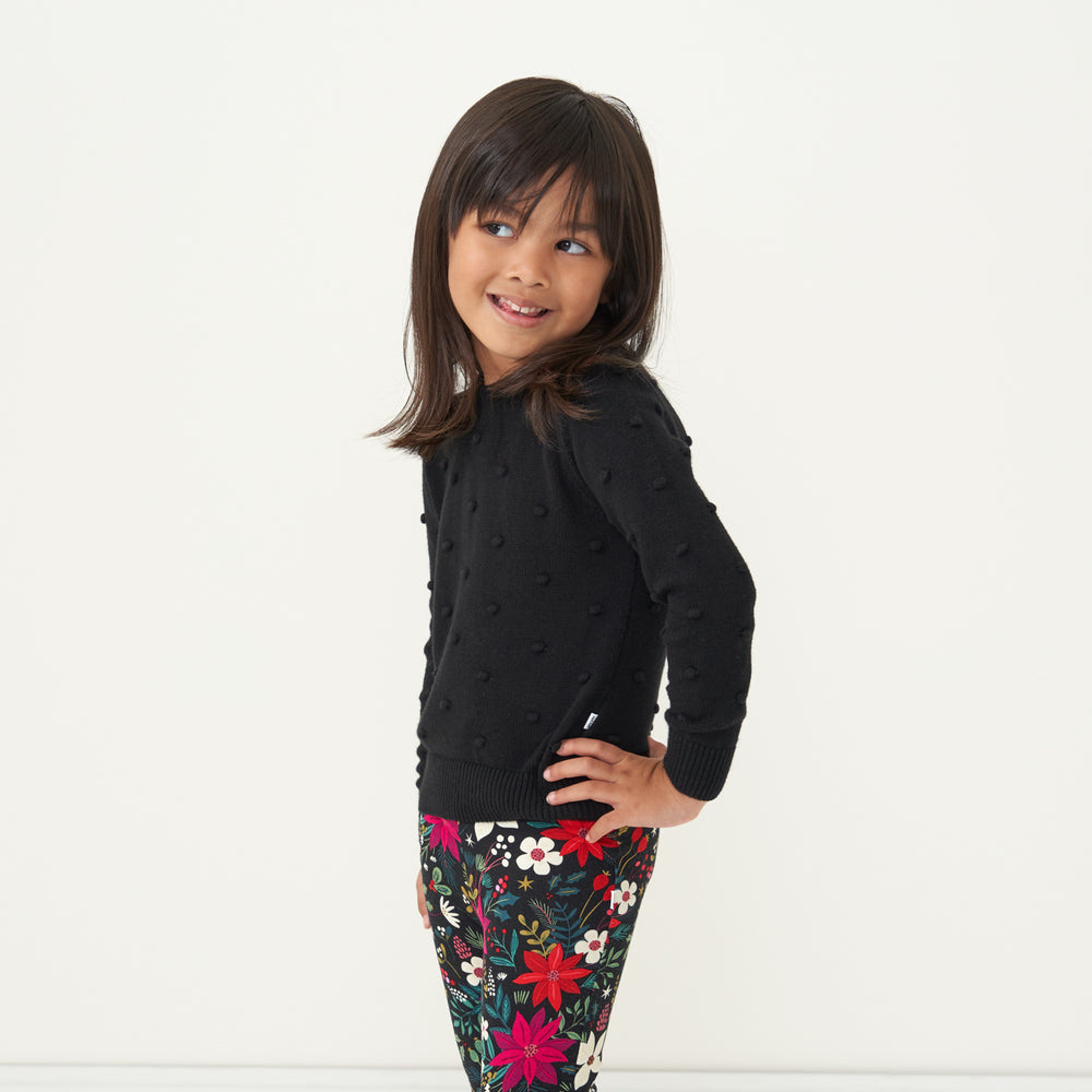 Child with her hand on her hip wearing a Black pom pom sweater and coordinating Berry Merry leggings
