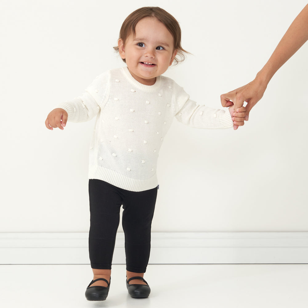 Child holding a parent's hand wearing an Ivory pom pom sweater