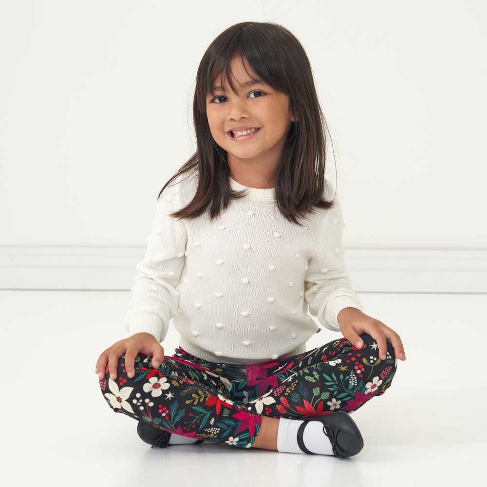 Child sitting on the floor wearing an Ivory pom pom sweater and coordinating Berry Merry leggings