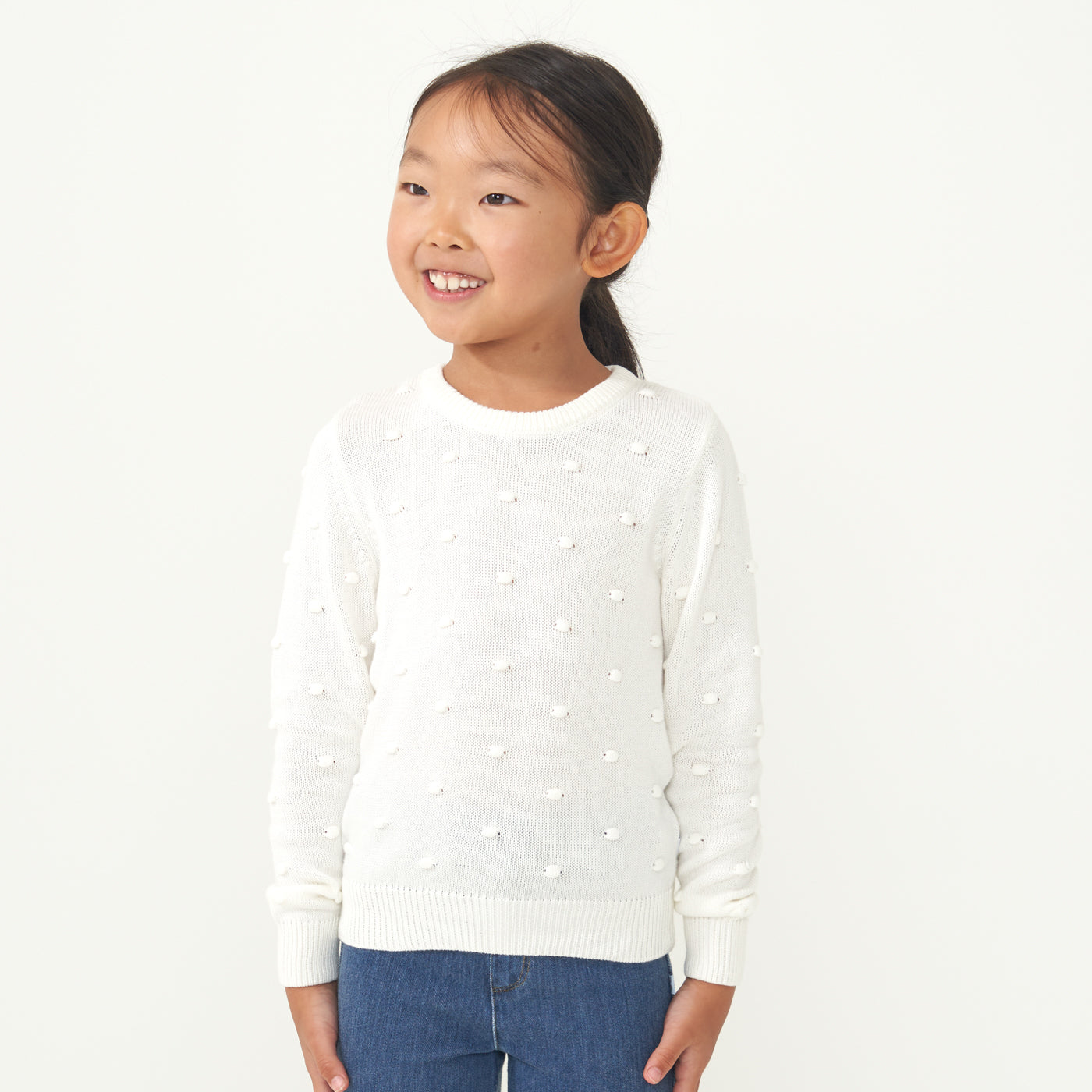 Child looking to the side wearing an Ivory pom pom sweater