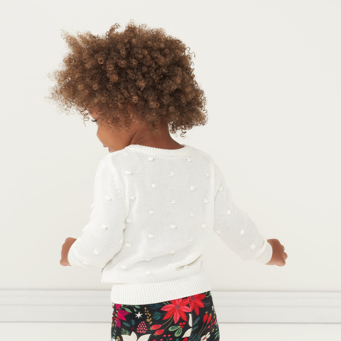 Back view image of a child wearing an Ivory pom pom sweater