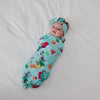 Aerial view of baby wrapped in the Disney & Pixar Christmas Village Swaddle & Luxe Bow Headband Set