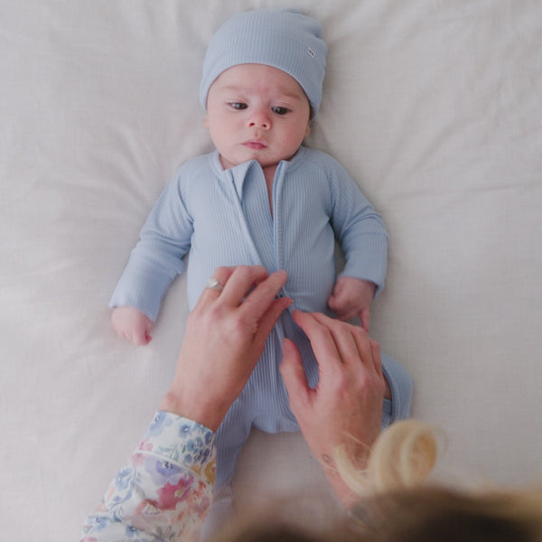 Infant laying on a bed wearing a Light Fog Ribbed Zippy