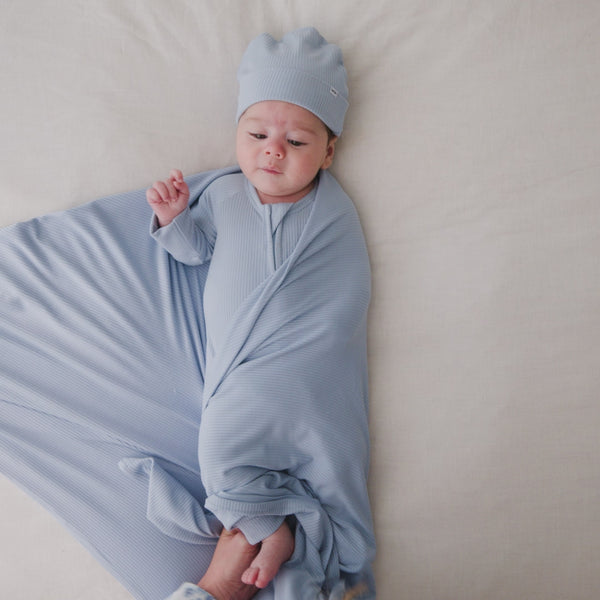 Mother wrapping baby in the Light Fog Baby Ribbed Swaddle & Infant Beanie Set