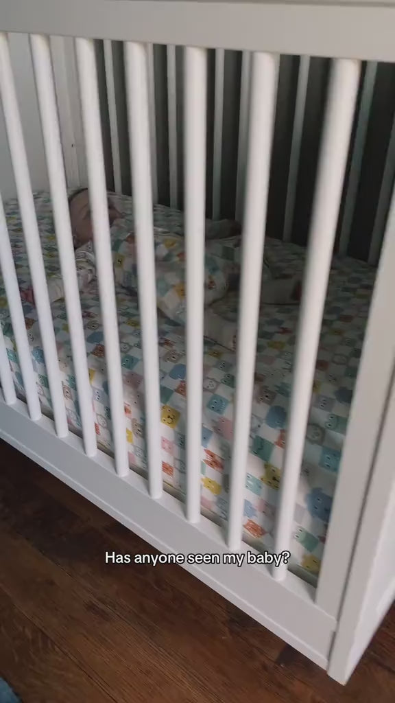 Infant laying in a crib, wearing a Check Mates Zippy