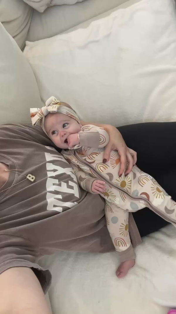 Baby being held by their mother, wearing a Desert Sunrise Zippy and Luxe Bow Headband