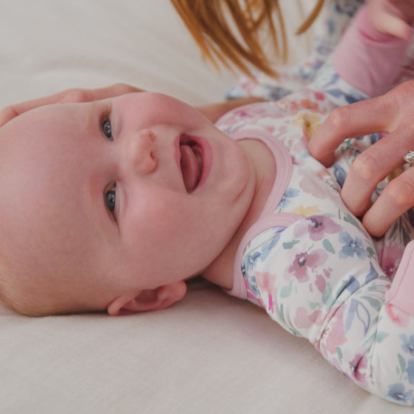 Newborn on a bed wearing the Tiny Blooms Crescent Zippy