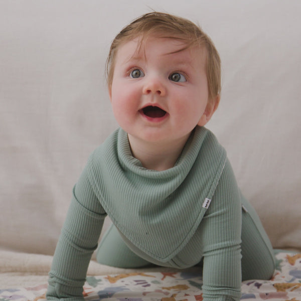 Baby wearing the Willow Baby Ribbed Bandana Bib with the matching newborn zipper pajamas
