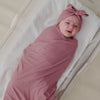 Aerial view of baby wearing the Rosewood Ribbed Swaddle & Luxe Bow Headband Set