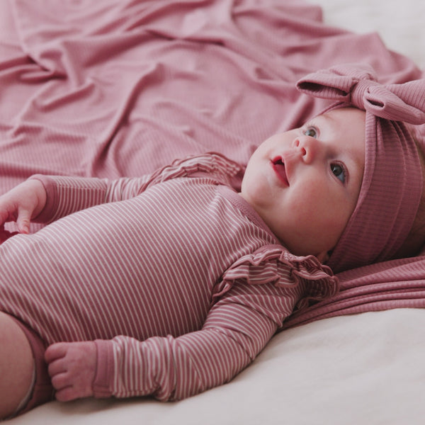 Newborn wearing the Rosewood Stripe Flutter Bodysuit laying on a matching baby blanket