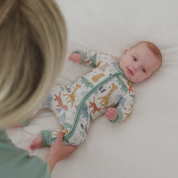 Baby laying on a bed wearing a Sweet Safari Zippy