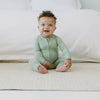 Video of a child sitting in front of a bed wearing a Heather Sage Zippy