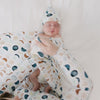 Child being swaddled by their mother in a Luna Neutral swaddle and hat set