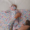 Adult swaddling a newborn in the Tiny Blooms Swaddle & Luxe Bow Headband Set