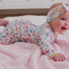 Baby laying on a bed wearing the Tiny Blooms Ruffle Zippy and matching luxe bow headband 