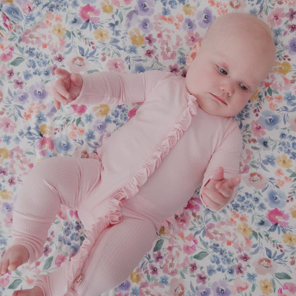 Newborn laying on a floral baby blanket wearing the Prima Pink Ribbed Ruffle Zippy 
