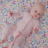 Newborn laying on a floral baby blanket wearing the Prima Pink Ribbed Ruffle Zippy 