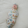 Baby swaddled in the Sweet Safari Swaddle & Infant Beanie Set on a white bed