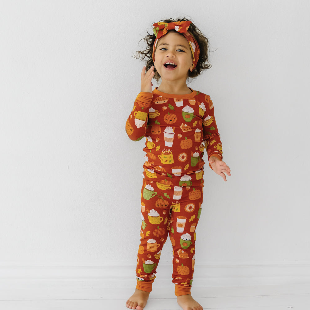 Child wearing a Pumpkin Spice two-piece pajama set and matching luxe bow headband