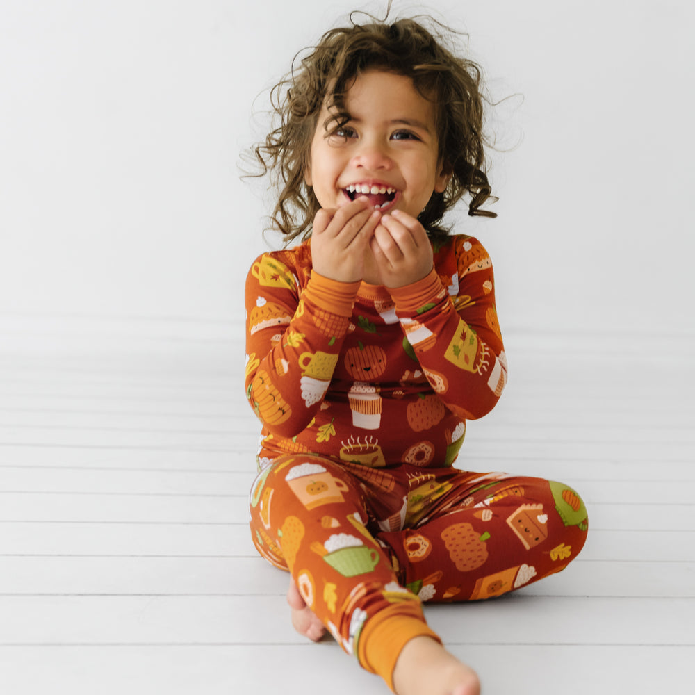 Child sitting on the ground wearing a Pumpkin Spice two-piece pajama set