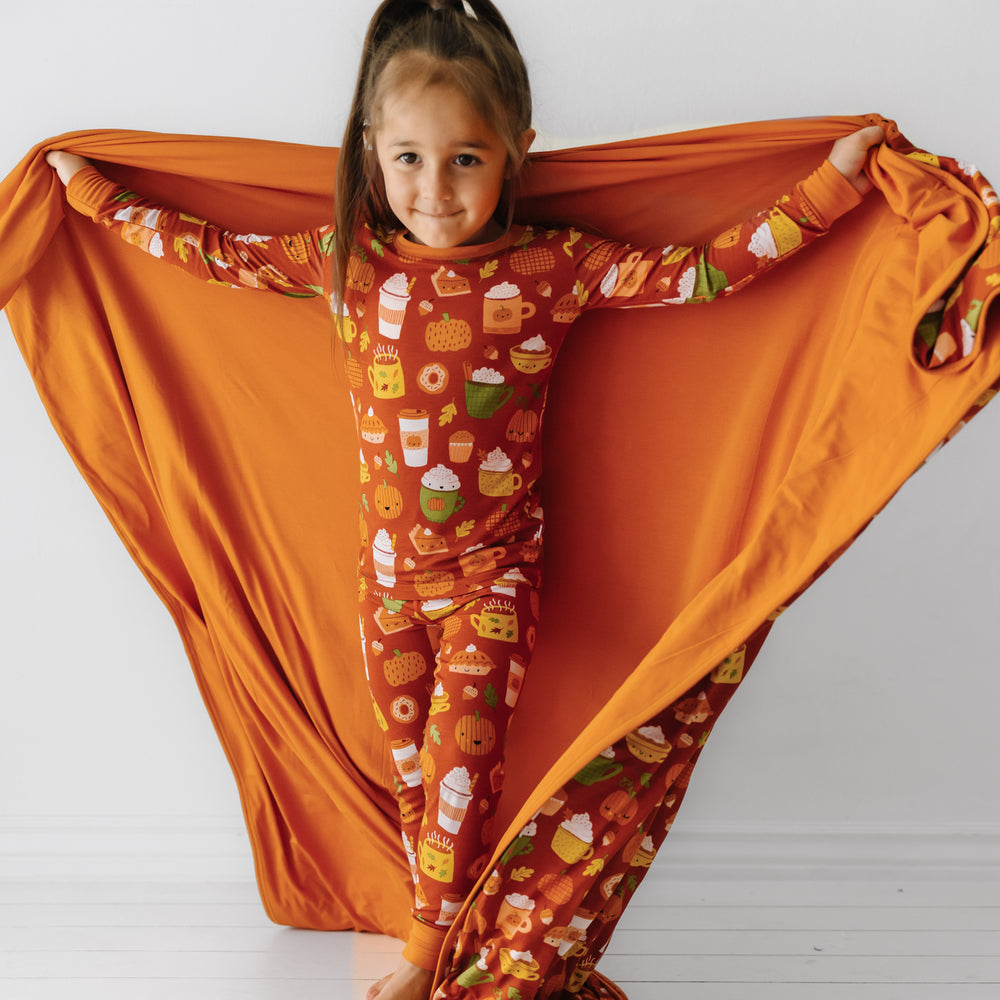 Child holding out a Pumpkin Spice large cloud blanket showing the solid orange backing