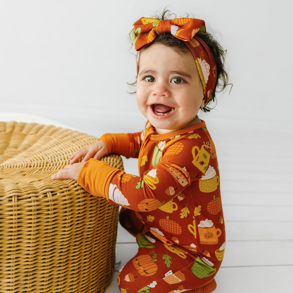 Child sitting next to a basket wearing a Pumpkin Spice luxe bow headband and matching zippy