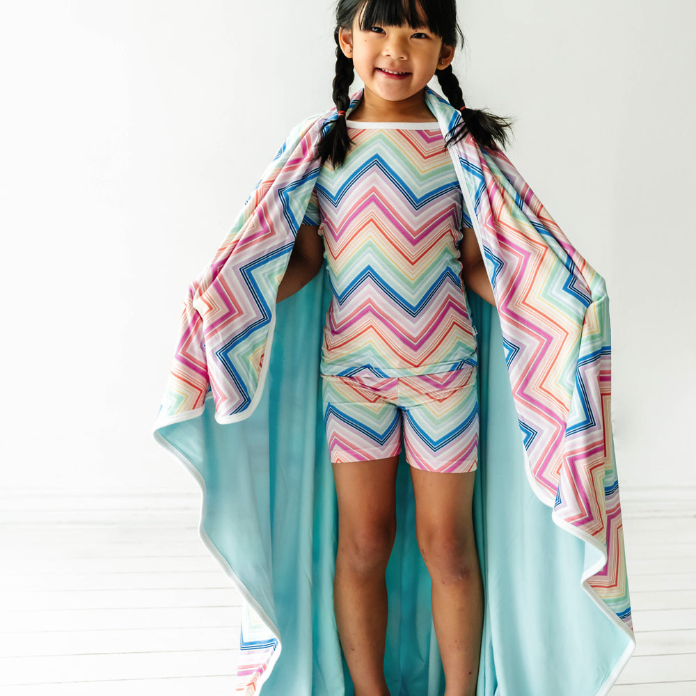 Child wrapped up in a Rainbow Chevron printed cloud blanket showing the solid aquamarine backing