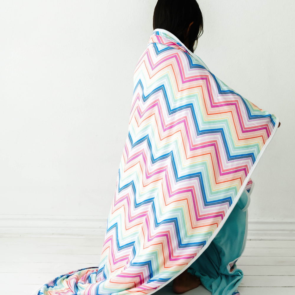 Back view of a child wrapped up in a Rainbow Chevron printed cloud blanket