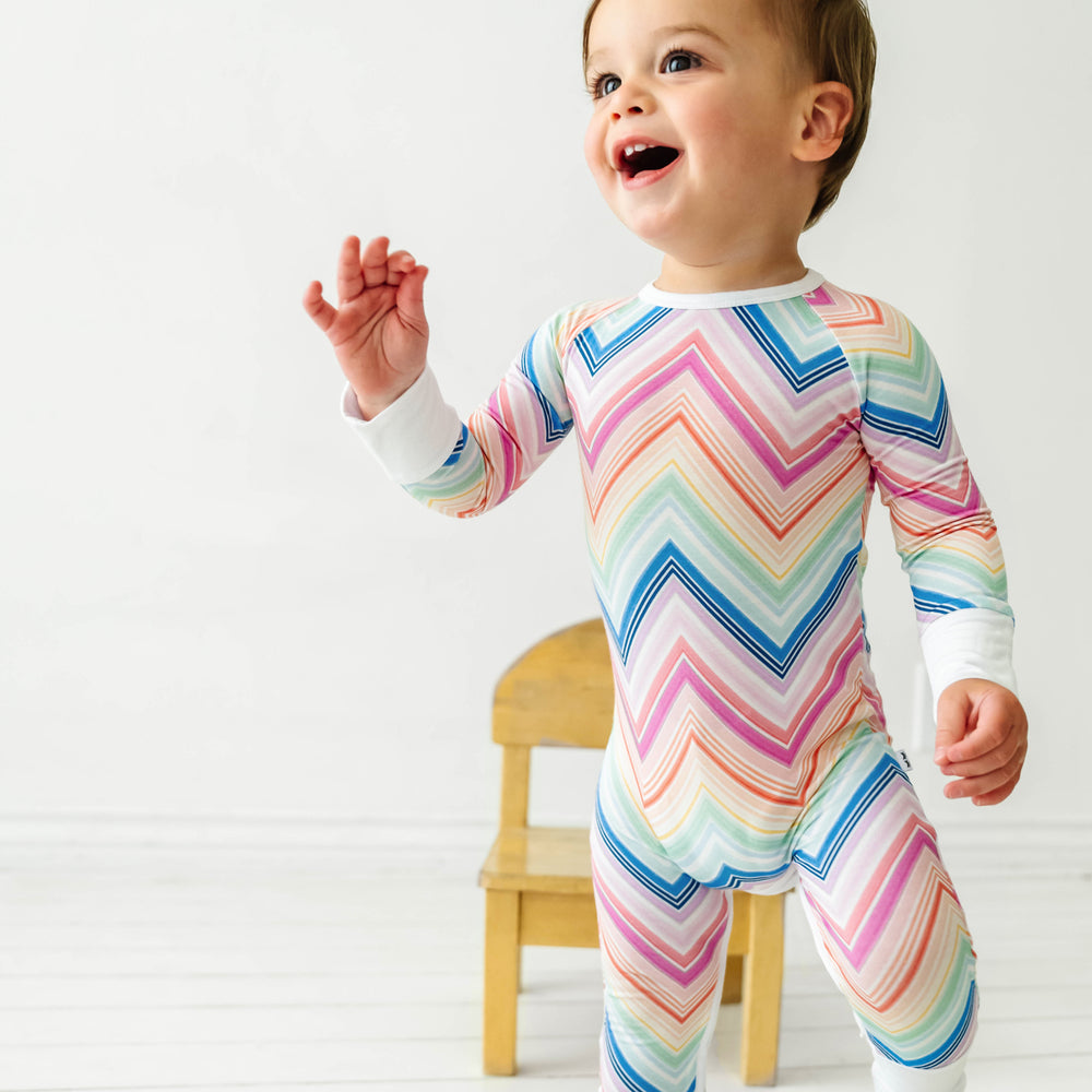 Child standing in front of a chair wearing a Rainbow Chevron printed crescent zippy