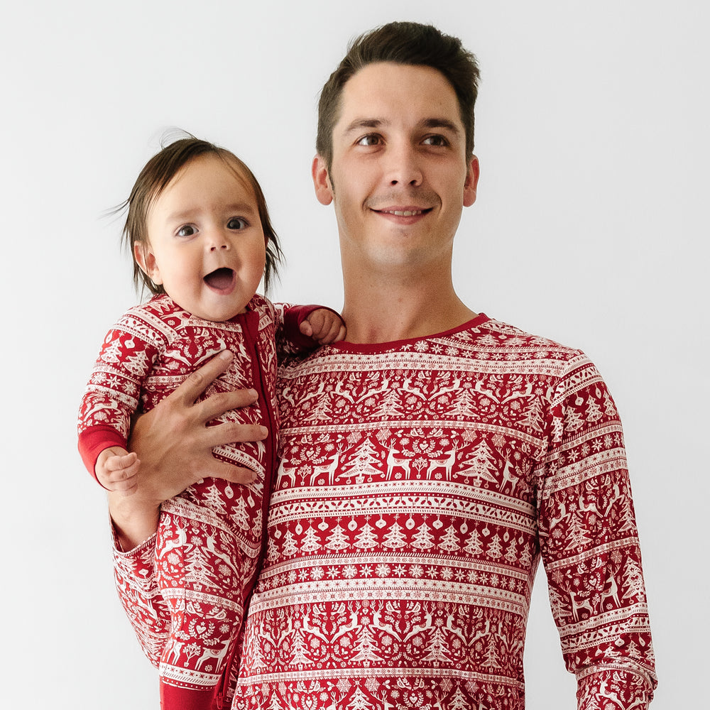 Man holding his daughter. He is wearing Reindeer Cheer men's pajama pants and matching pajama top. His daughter is wearing a matching Reindeer Cheer zippy